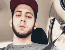 a man with a beard wearing a hat and a seat belt looks at the camera