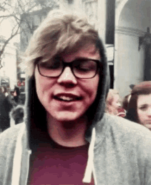 a young man wearing glasses and a hooded sweatshirt is smiling