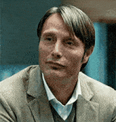 a close up of a man in a suit and sweater looking at the camera .