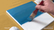 a person is painting a blue and white canvas with the words made in animotica on the bottom