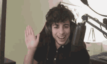 a young man wearing headphones is sitting in front of a microphone waving his hand .