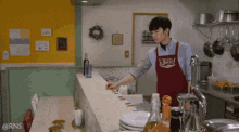 a man wearing a red apron that says jurri is standing in a kitchen