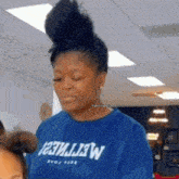 a woman in a blue t-shirt is standing in a room with her hair in a bun .