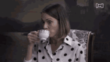 a woman in a polka dot shirt drinking from a cup