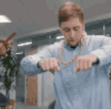 a man wearing a blue shirt and a gold chain around his neck is standing in an office .