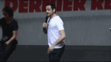 a man in a white shirt is dancing on a stage in front of a sign that says derrick ke