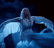 a woman in a white dress has her arms outstretched in the dark