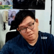 a man wearing glasses and a blue shirt with the word tach on his chest .