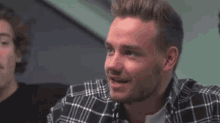a man in a plaid shirt is smiling and looking at the camera while sitting next to another man .