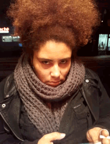 a woman wearing a scarf and a black jacket looks at her phone