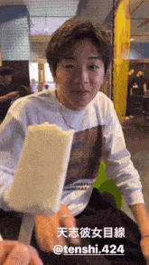 a man wearing a white shirt with a picture of a car on it is holding an ice cream bar