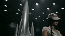 a woman wearing a hat is standing in front of a silver object