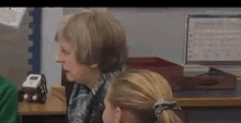 a woman is talking to a girl in a classroom while sitting at a desk .