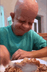 a bald child is eating spaghetti with a fork and knife