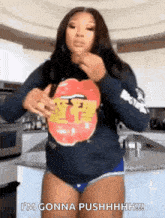 a woman is standing in a kitchen wearing a shirt that says `` i 'm gonna pushhhh '' .