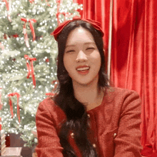 a woman wearing a red headband and a red jacket smiles in front of a christmas tree