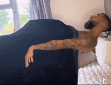 a man is laying on a bed with his arms outstretched and a black blanket on his back .