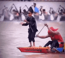 a man in a red shirt is paddling a boat while a boy in a black hat stands on a boat