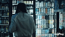 a person standing in front of a fridge full of cans and bottles of beer