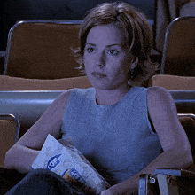 a woman sits in a theater holding a bag of popcorn