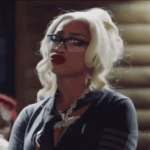 a blonde woman wearing glasses and red lipstick is looking at the camera .