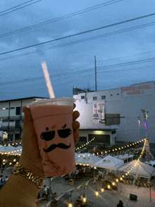 a person holding a cup with a mustache on it in front of andre hotel manila