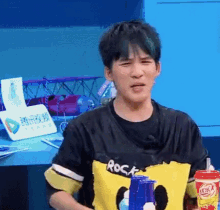 a young man wearing a shirt that says rock on it is holding a can of soda .