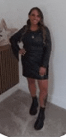 a woman in a black dress and black boots is standing in front of a white wall .