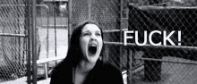 a black and white photo of a woman screaming in front of a chain link fence with the word fuck written on it
