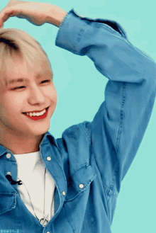 a young man wearing a blue denim shirt making a heart shape with his hands