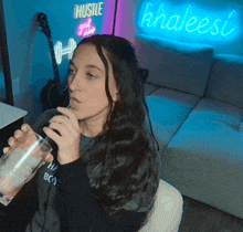 a woman is drinking from a glass in front of a neon sign that says hustle