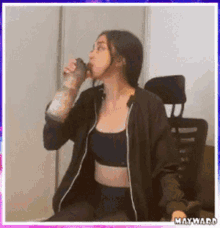 a woman in a black jacket is drinking from a shaker .
