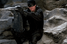 a man wearing a black mask and gloves is sitting on a rock