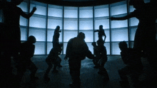 a group of people are dancing in a dark room with blue lights behind them