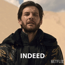 a man with a beard is standing in front of a sign that says indeed on it