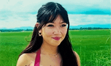 a woman in a pink top is standing in a field of grass .