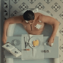 a man is laying in a bathtub with a plate of food and a book