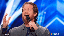 a man with a beard is singing into a microphone with the nbc logo in the corner