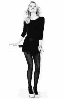 a woman in a black dress is dancing with her arms outstretched