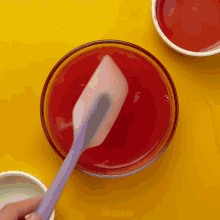 a person is using a spatula to mix red liquid in a bowl .