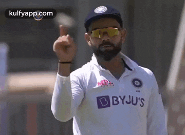 a cricket player wearing sunglasses and a white shirt is giving a thumbs up .