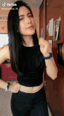 a woman in a black crop top and black pants is standing in front of a wall .