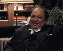 a man in a suit and tie is smiling and sitting in front of a lamp