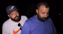 a man wearing a nike shirt stands next to another man wearing a hat with a dolphin on it
