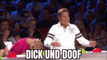 a man is standing in front of a crowd with a woman laying on the floor and a sign that says dick und doof .