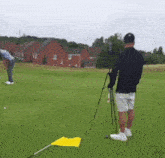 a man is standing on a golf course watching another man putt a ball