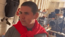 a man wearing a red scarf around his neck is standing in a cluttered room .