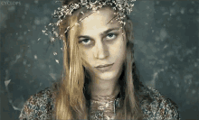 a woman with long blonde hair and a flower crown on her head looks at the camera