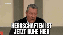 a man in a suit and tie is sitting in front of a microphone and says herrenschaften ist jetzt ruhe hier