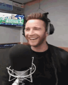 a man wearing headphones is smiling in front of a microphone with the big show on a television behind him